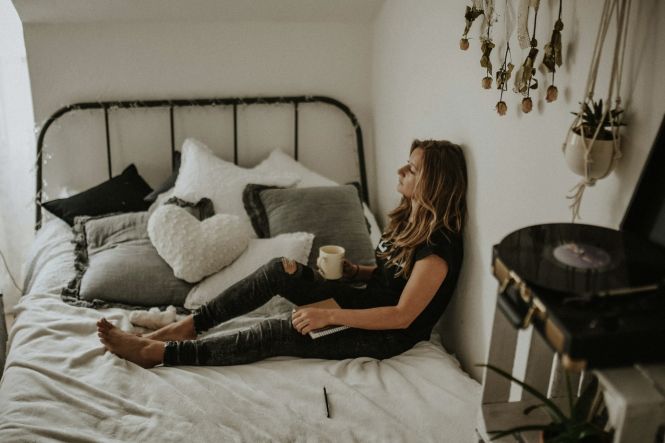 A woman leaning on wall while sitting on bed. Photo by Kinga Howard on Unsplash